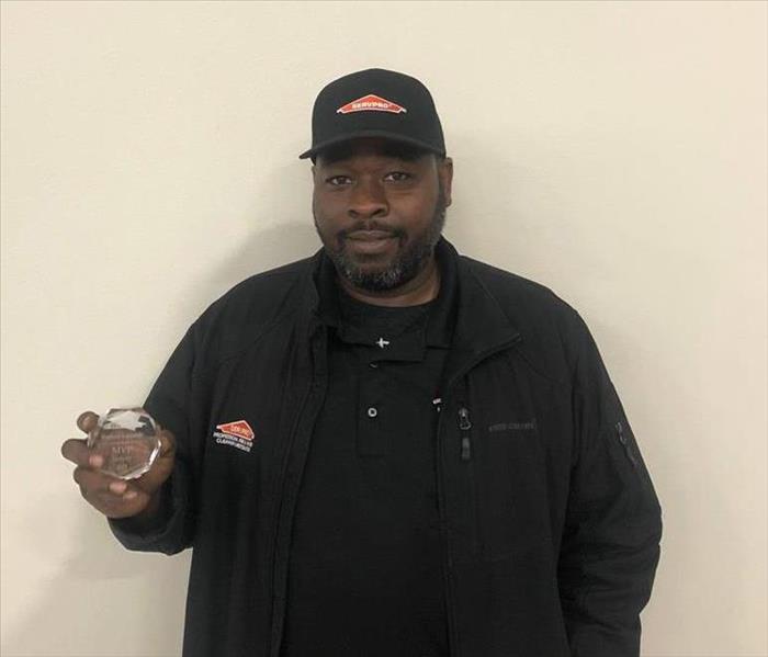 a man holding an award in front of a beige wall